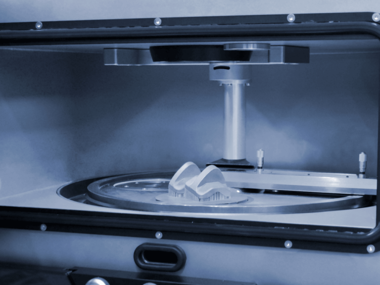 Close-up view of a 3D printer in operation, showcasing the creation of a complex object on a circular build platform with a vertical support structure above it.